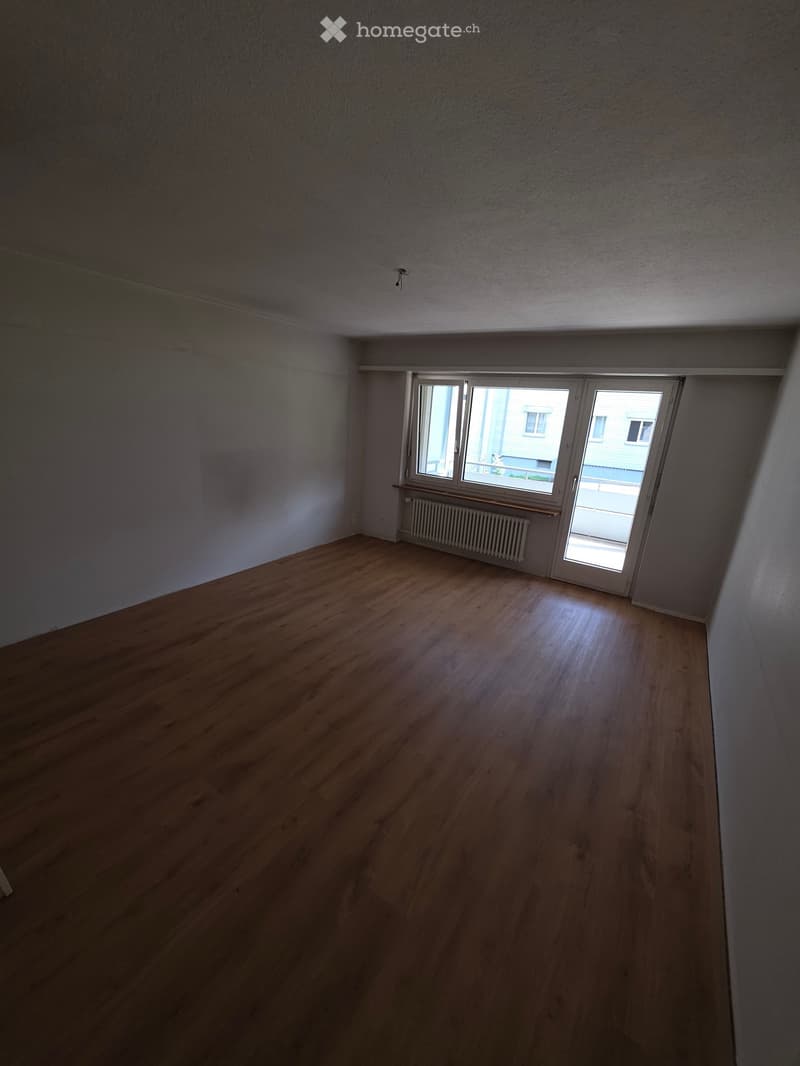 Empty room with wooden flooring, white walls, and a window with a radiator below it.