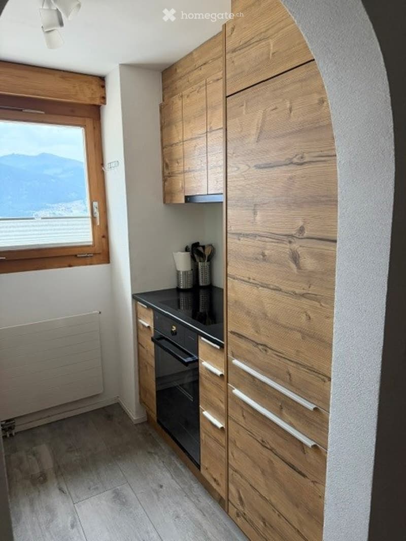 Modern kitchen with wooden cabinets, black countertop, built-in oven, and a view of mountains through a window.