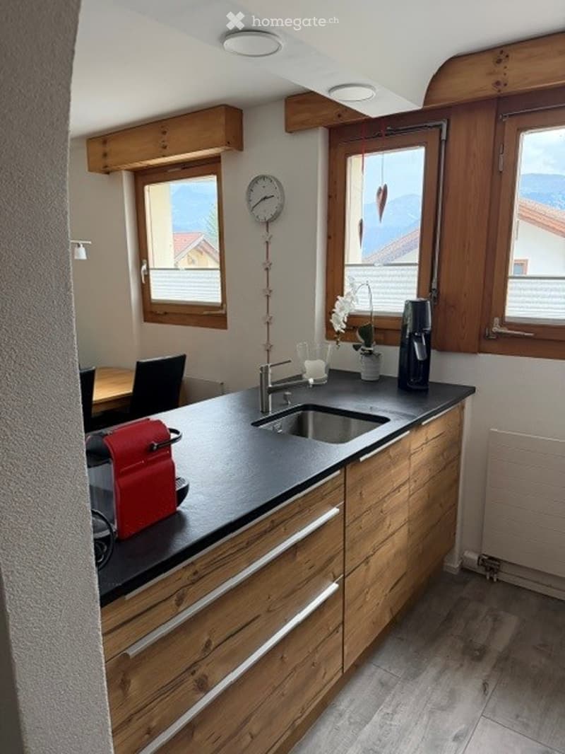 Modern kitchen with wooden cabinets, black countertop, stainless steel sink, coffee maker, and a small dining area with a table and chairs.