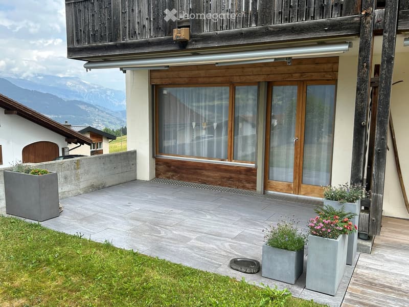 Outdoor patio area with grey planters, wooden decking, and a view of mountains in the background.