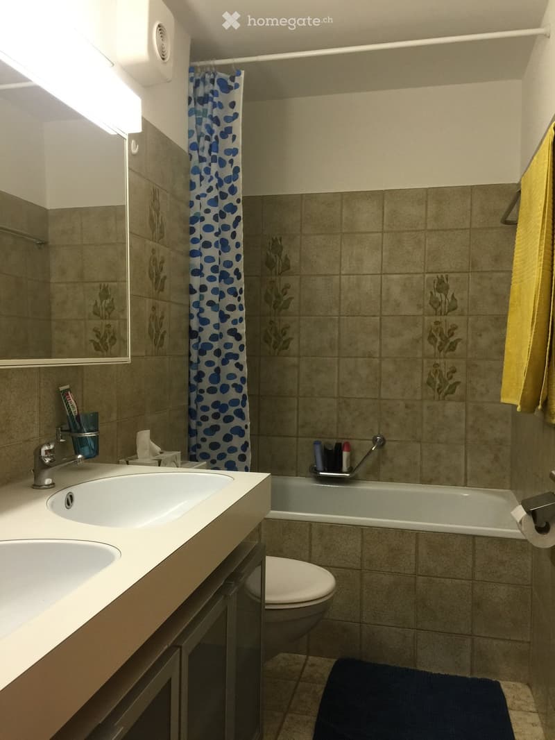 Bathroom with a double sink, mirror, toilet, bathtub, and a shower curtain with blue polka dots. A yellow towel hangs on the side.