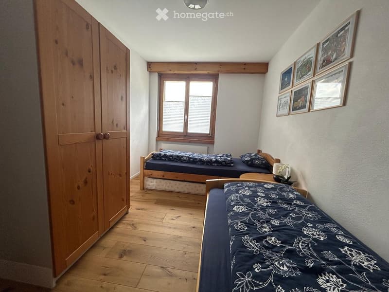 Cozy bedroom with wooden floors, three single beds, a wardrobe, and framed pictures on the wall.