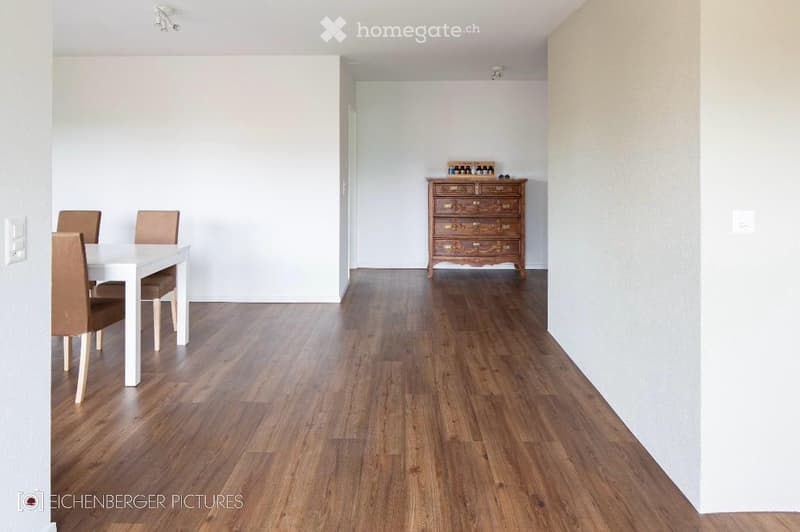 Spacious dining area with light wooden flooring, white dining table, four chairs, and a wooden chest of drawers with decorative items on top.