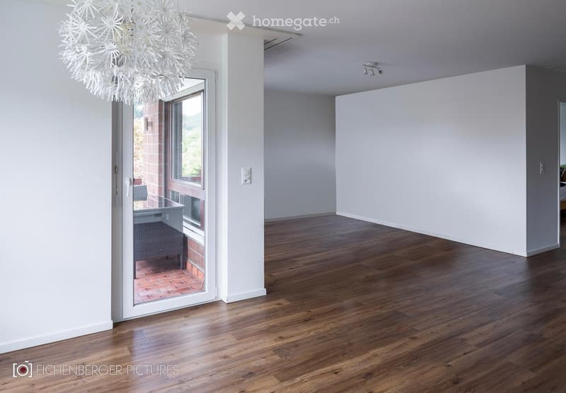 Empty room with wooden flooring, white walls, and a large glass door leading to an outdoor area. A decorative chandelier hangs from the ceiling.