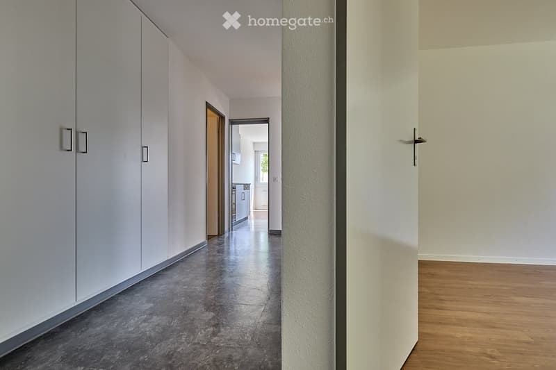 Empty hallway, wooden floor, large wardrobes on left, doors to kitchen and bathroom visible in the background