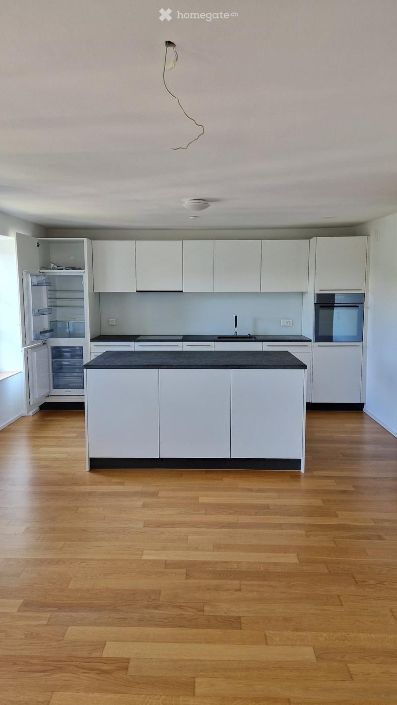 Modern kitchen with white cabinets, black countertop, wooden flooring, and stainless steel appliances including a refrigerator and oven.
