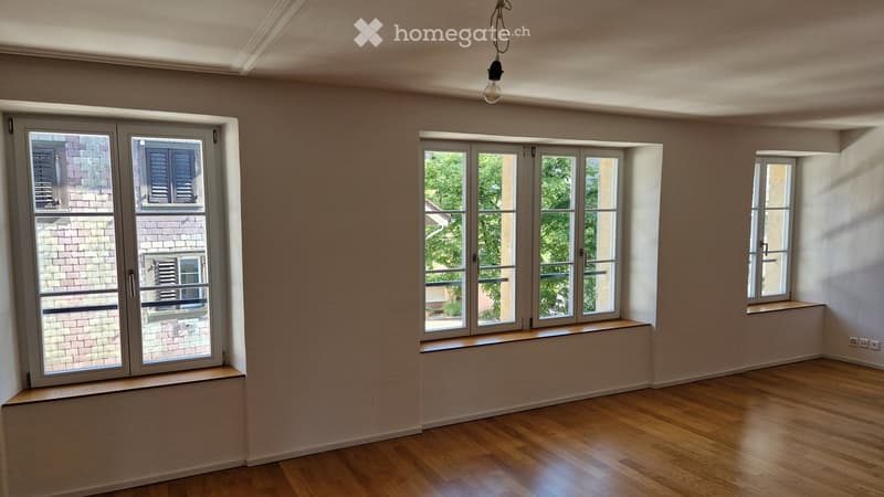 Empty room with wooden flooring, large windows, and built-in window seats. No furniture or equipment present.