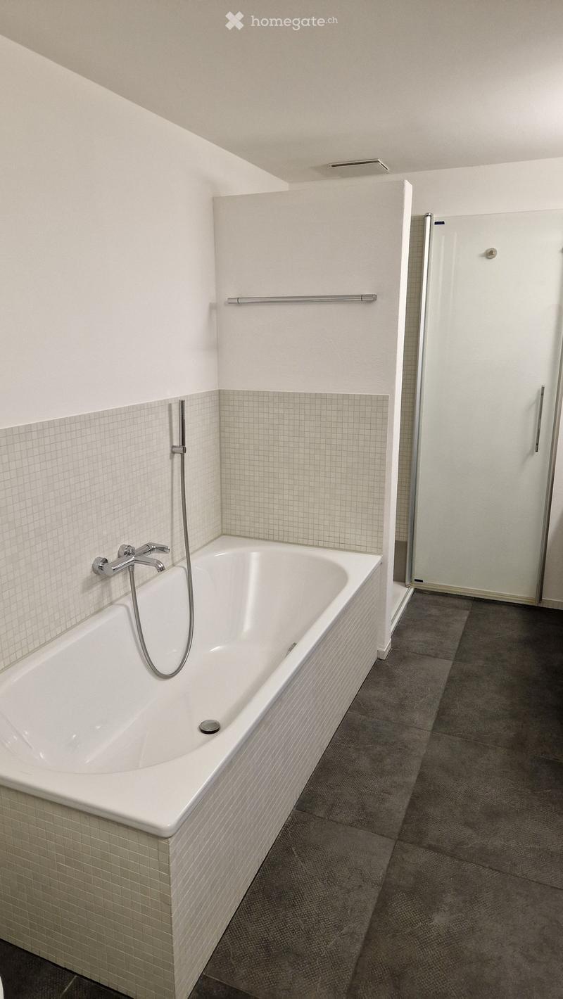 Modern bathroom with a white bathtub, tiled walls, and a glass shower enclosure.