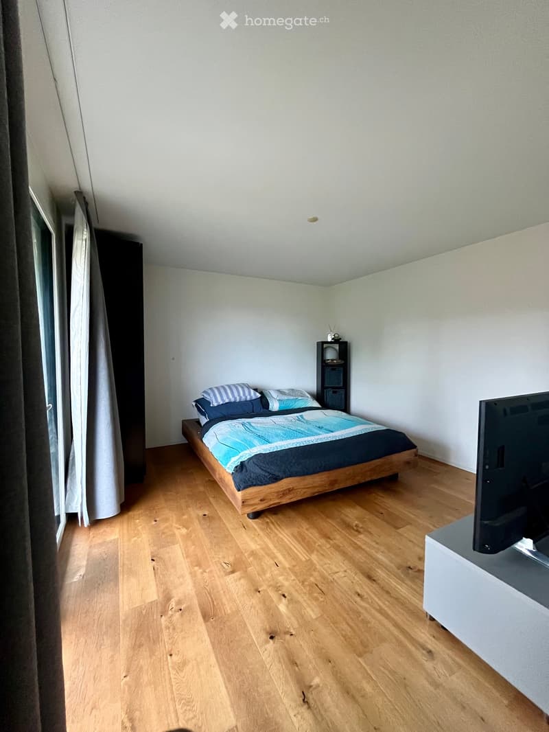A modern bedroom with wooden flooring, a bed with blue and white bedding, a nightstand, and a television on a stand.