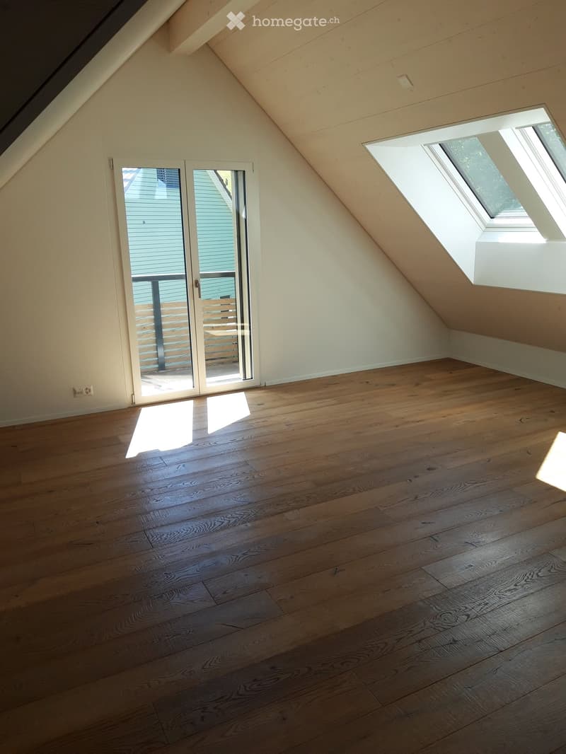 Empty attic room with wooden flooring, skylight windows, and a sliding glass door leading to a balcony.