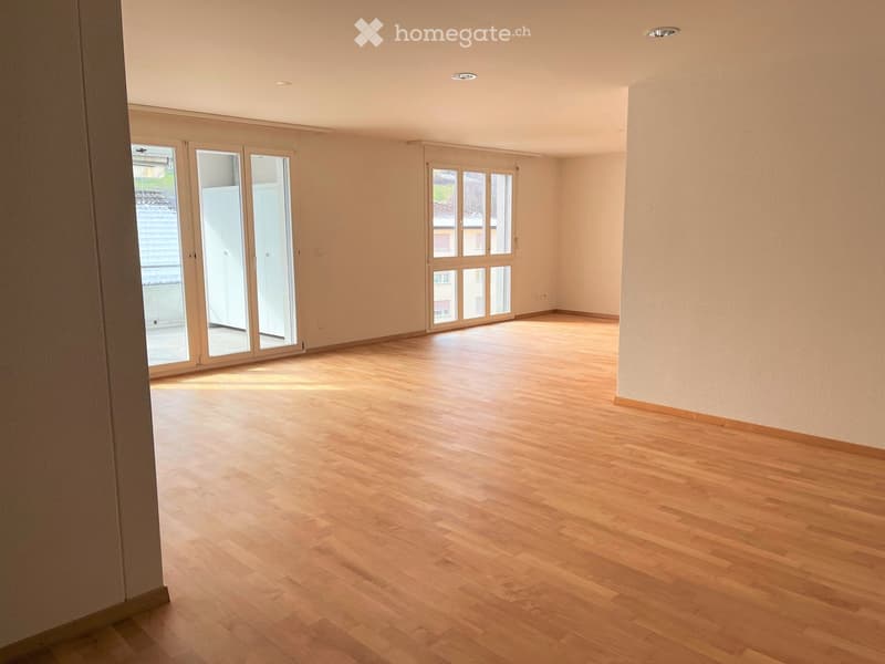 Empty room with wooden flooring, large windows, and neutral-colored walls.