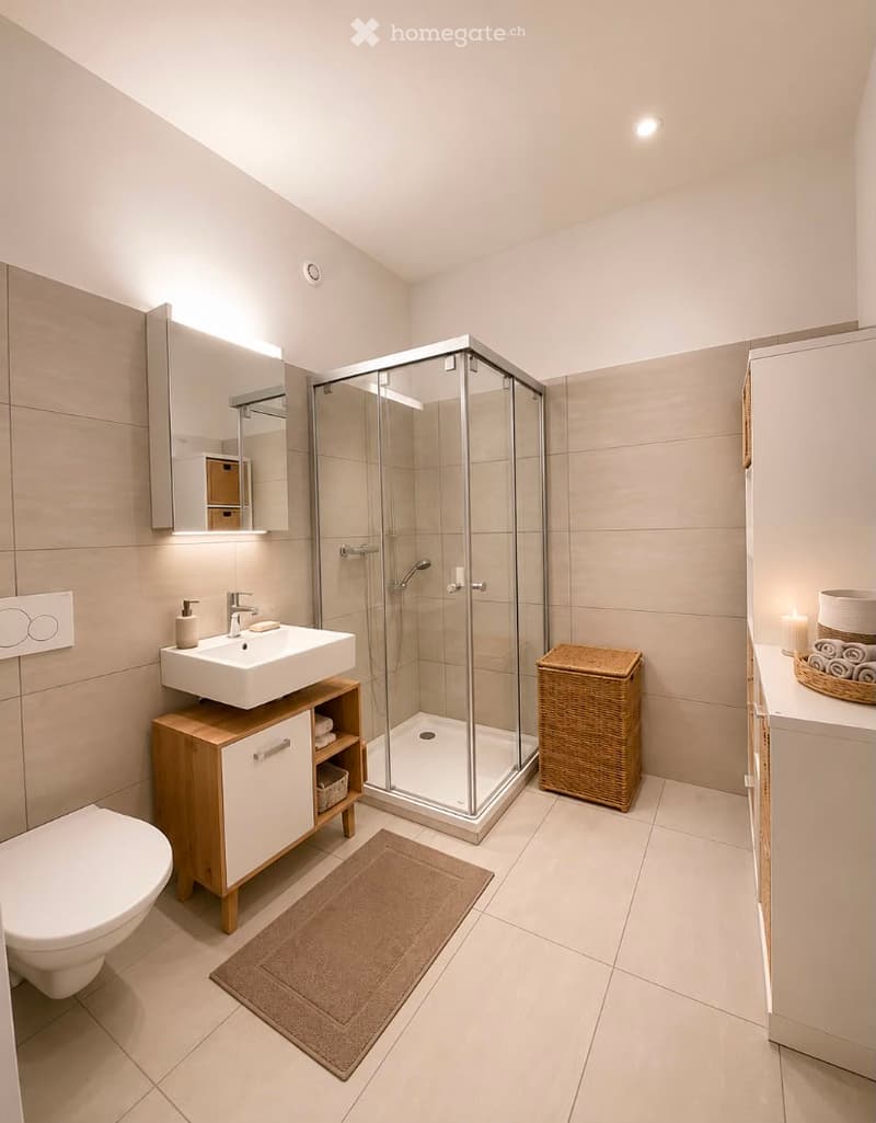 Modern bathroom with a white sink, toilet, shower, and a wicker basket on the floor. The walls are tiled, and there is a mirror above the sink.