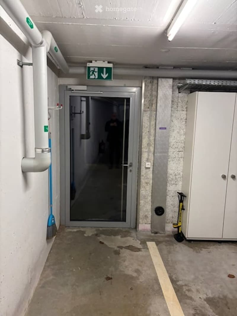 Entrance to a garage with a glass door, a white cabinet, and a broom