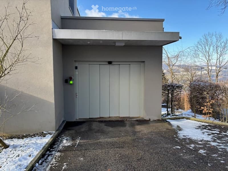 Building with a garage entrance, white doors, and a control panel with a green light