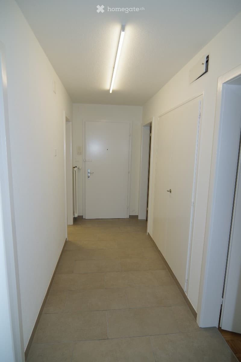 Empty hallway with beige tiled floor, white walls, and several closed doors.