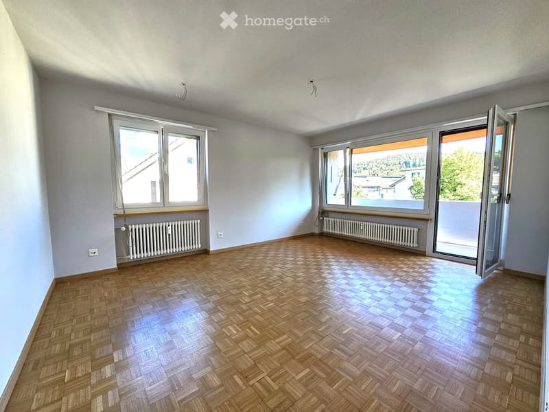Empty room with wooden herringbone flooring, large windows, radiators, and an open sliding door leading to a balcony.
