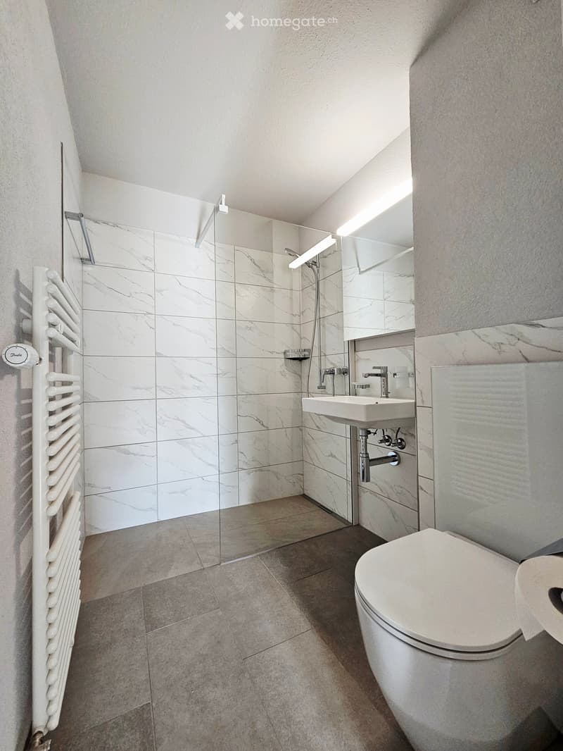 Modern bathroom with marble tiles, a white radiator, a glass-enclosed shower, a sink, and a toilet.