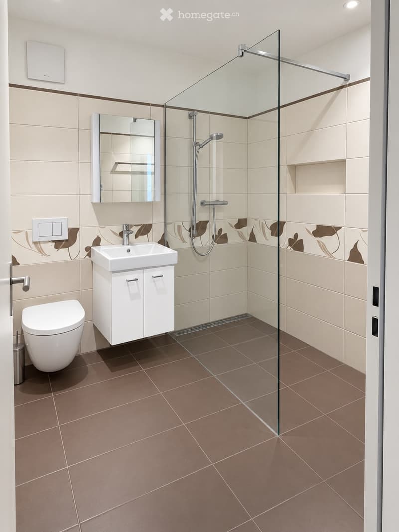 Modern bathroom with beige tiles, a white toilet, a white sink with a cabinet, a mirror, and a glass-enclosed shower area.