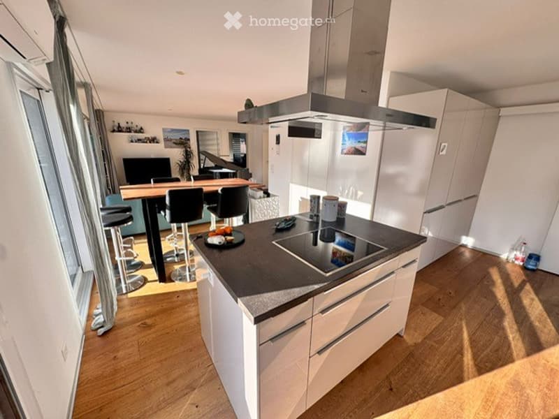 Modern kitchen with white cabinets, island, induction cooktop, stools, table, chairs, and a piano in the background.