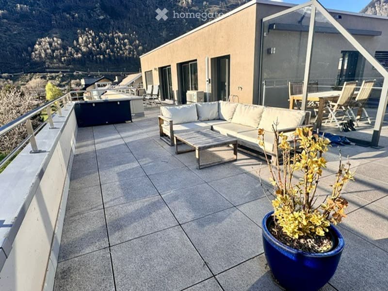 Spacious outdoor terrace with modern furniture, including a sofa, coffee table, and dining area, overlooking a scenic mountain view.