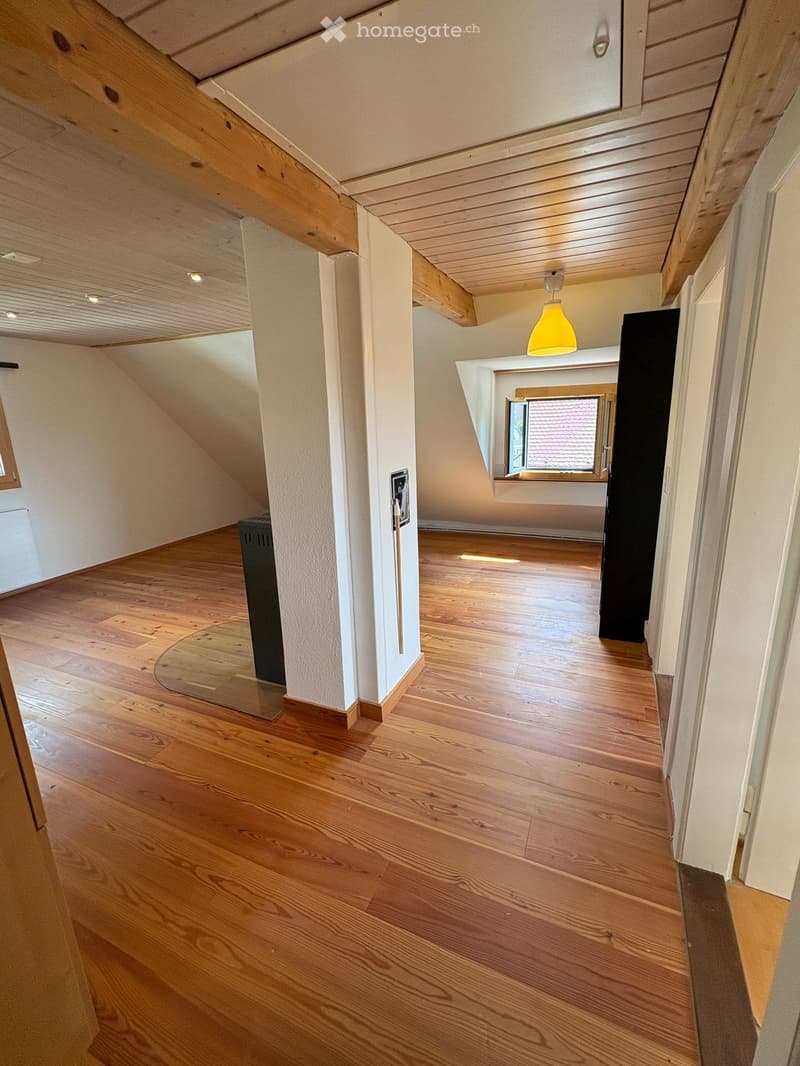 Spacious hallway with wooden flooring, white walls, and exposed wooden beams on the ceiling. Features a pendant light and a small window at the end.