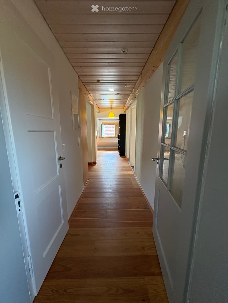 Wooden floor hallway with white walls, multiple doors, and a hanging light fixture.