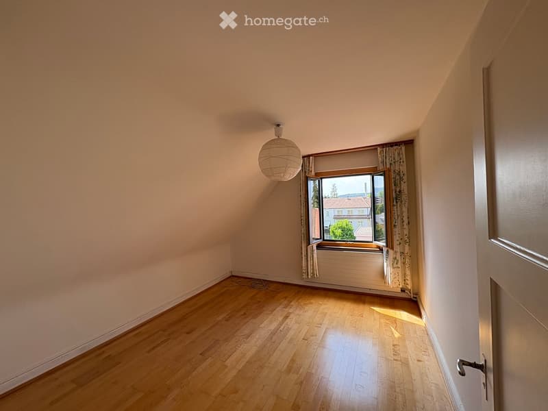 Empty room with wooden flooring, light-colored walls, a single window with curtains, and a hanging light fixture.