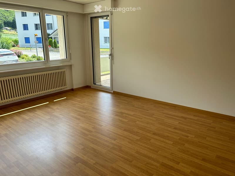 Empty room with wooden flooring, large windows, and a radiator. No furniture or equipment present.