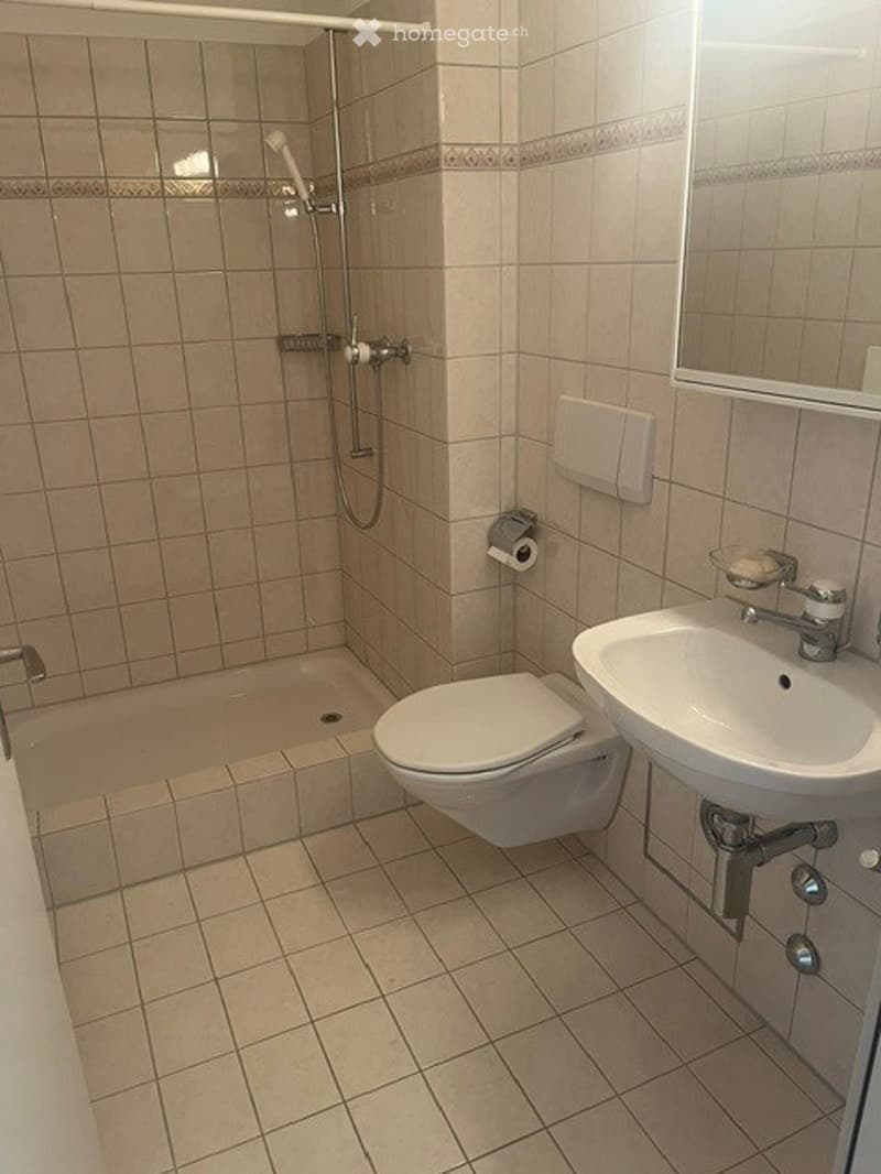 Modern bathroom with beige tiles, a toilet, a sink, a bathtub, and a shower area with a glass enclosure.