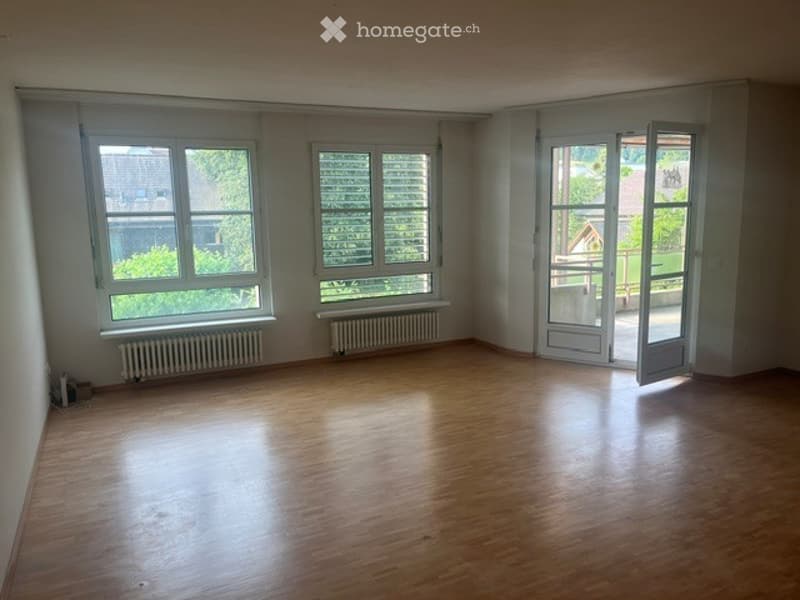 Empty room with wooden flooring, white walls, large windows, and a sliding glass door leading outside.