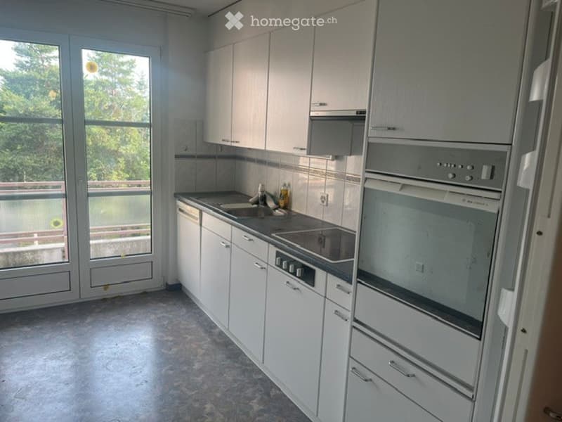Modern kitchen with white cabinets, stainless steel appliances, and a large window offering a view of the balcony.