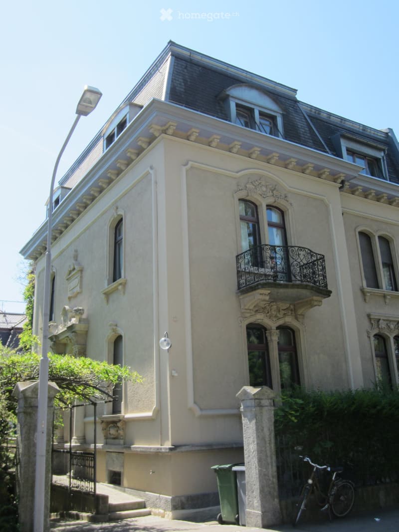 3 story house, beige paint, gray roof, black balcony railings, small garden, lamp on wall