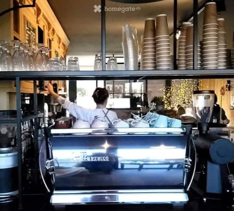 A modern coffee shop interior with a coffee machine, stacked cups, and a barista preparing drinks.