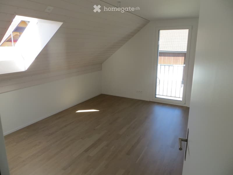 Empty attic room with wooden flooring, white walls, and a skylight window. The room features a sliding glass door leading to a balcony area.