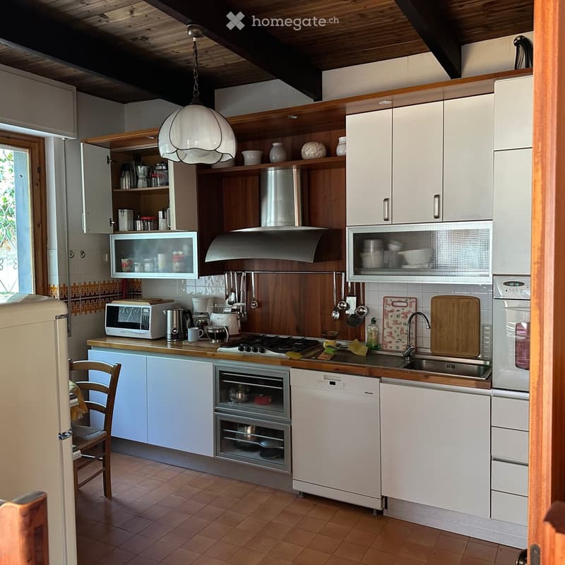 The kitchen features white cabinets, wooden countertops, and various appliances including a refrigerator, oven, dishwasher, and microwave. There is a sink with a faucet, wooden cutting boards, and a hanging pendant light. The floor is tiled, and there is