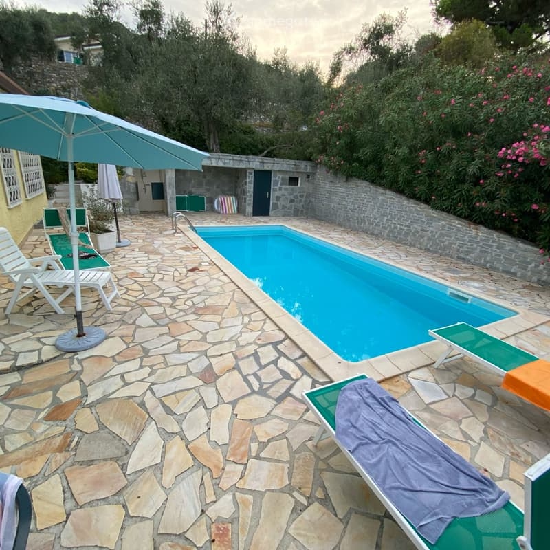 Outdoor area with a swimming pool, stone-paved ground, lounge chairs, and an umbrella.