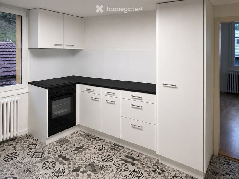 Modern kitchen with white cabinets, black countertop, and a built-in oven. The floor features a patterned tile design.