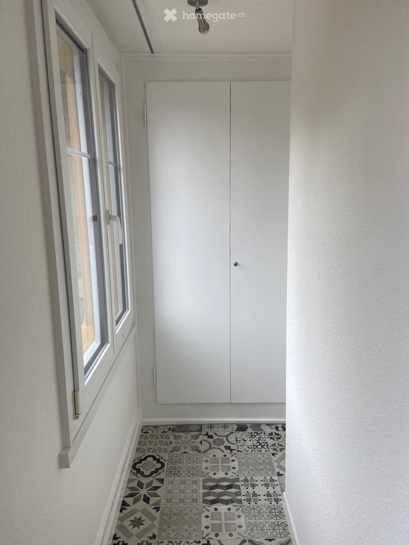 Balcony with white cabinet, large window, and patterned tile floor.