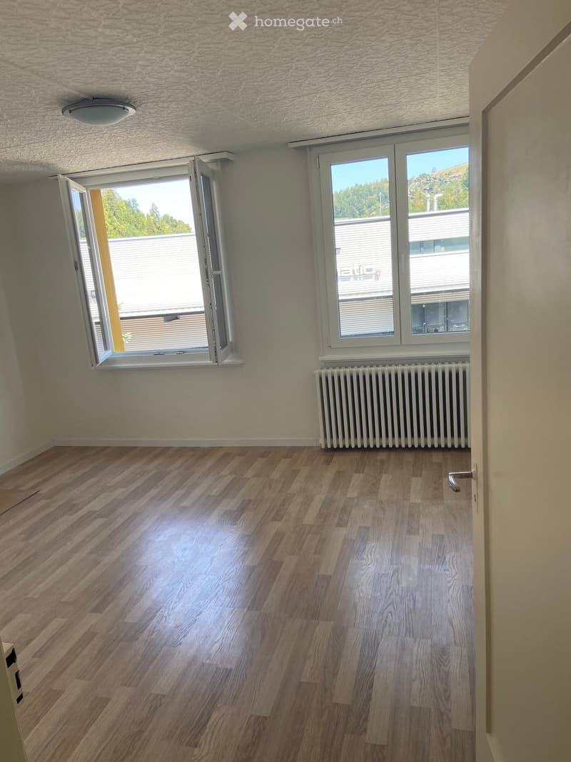 Empty room with wooden flooring, white walls, large windows, and a radiator. No furniture or equipment present.