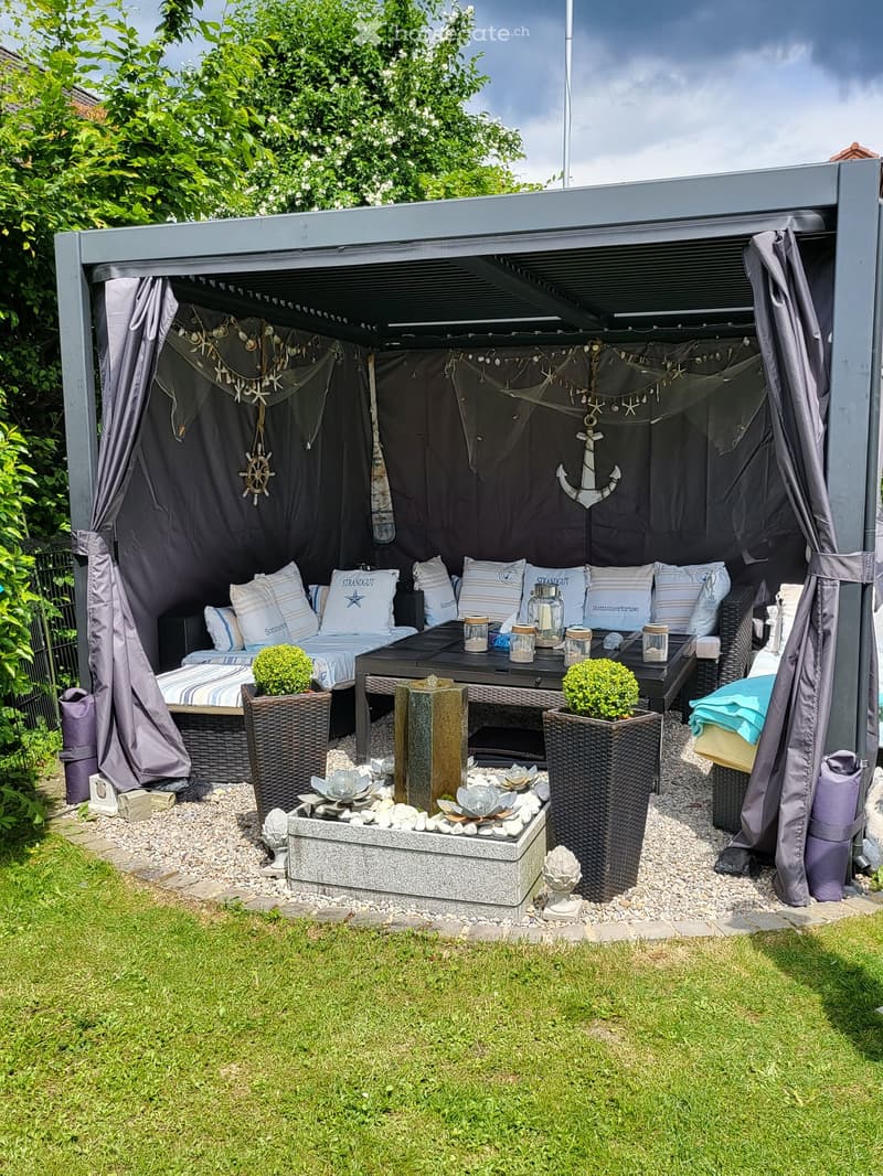 A cozy outdoor seating area with a sofa, table, and decorative elements, including potted plants and a small fireplace.