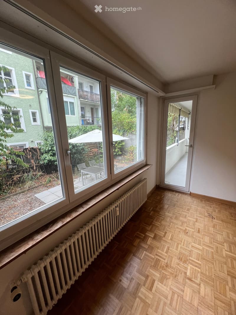 Empty room with wooden flooring, large windows, radiator, and a door leading to a balcony.