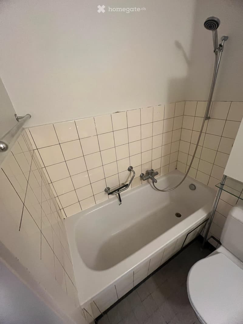 Bathroom with a bathtub, toilet, tiled walls, and a showerhead attached to the wall.