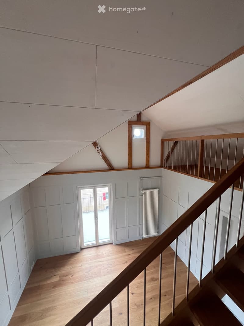 Spacious hallway with wooden flooring, white walls, and a staircase leading upwards. Features include a radiator, a window with a view, and a small skylight.