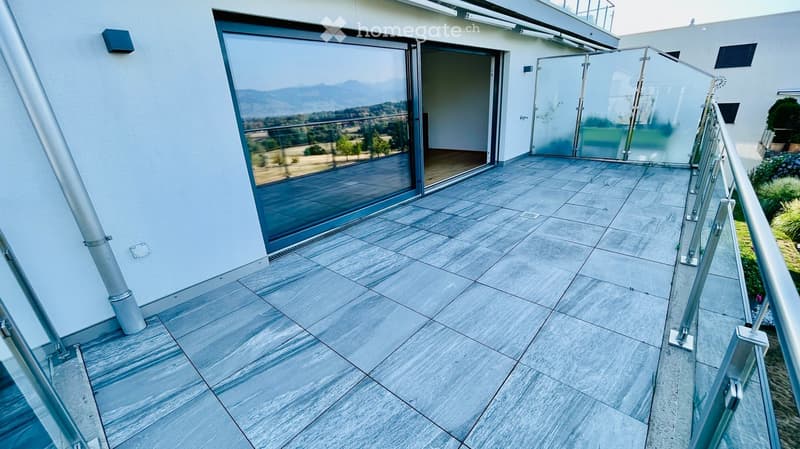 Modern balcony with large glass sliding doors, marble tiles, metal railing, and scenic mountain view.