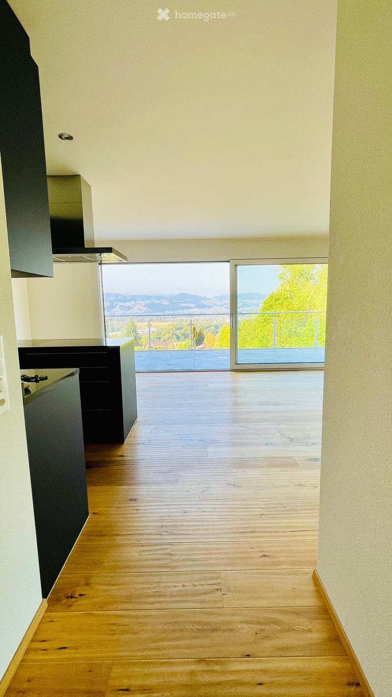 Empty room with wooden flooring, white walls, and large sliding glass doors leading to a balcony with a scenic mountain view.