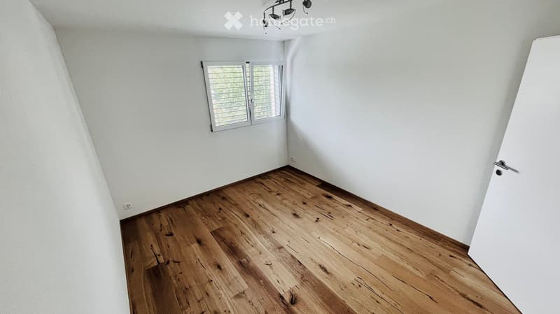 Empty room with wooden flooring and white walls, featuring a window with blinds and a door.