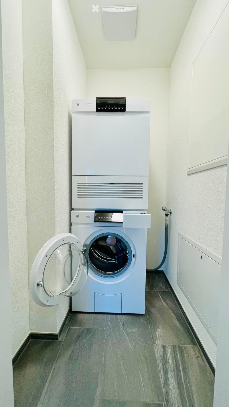 A compact bathroom with a stacked washing machine and dishwasher unit, featuring a modern design with white walls and grey tiled flooring.