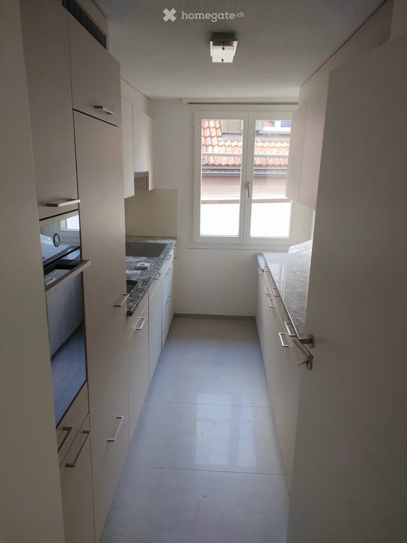 Modern and spacious kitchen with white cabinetry, granite countertops, integrated appliances, tiled flooring, and a window offering a scenic view.