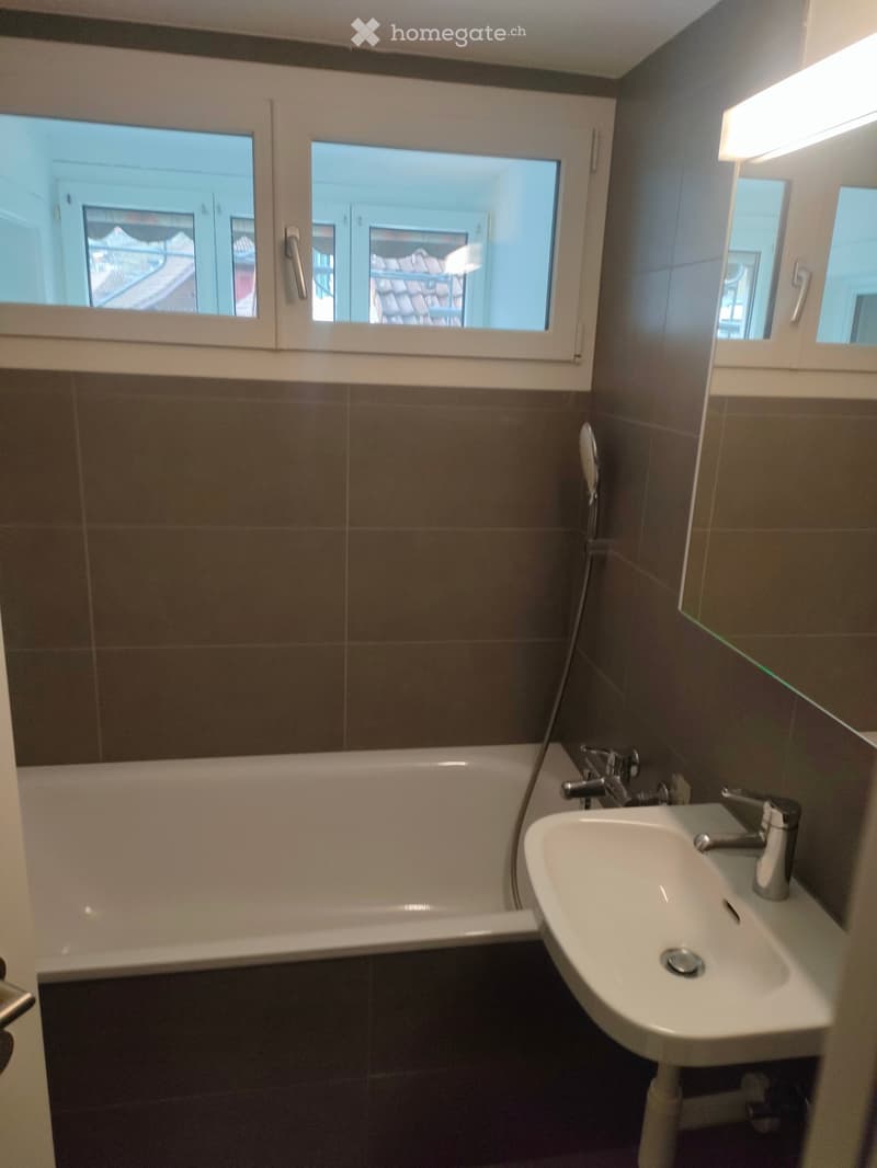 white bath, white sink, mirror above the sink, tiled walls, ceiling light