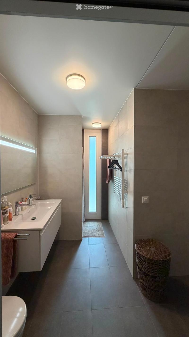 Modern bathroom with a sink, mirror, towel rack, and wicker basket. The space features a large window providing natural light and a sleek, contemporary design.